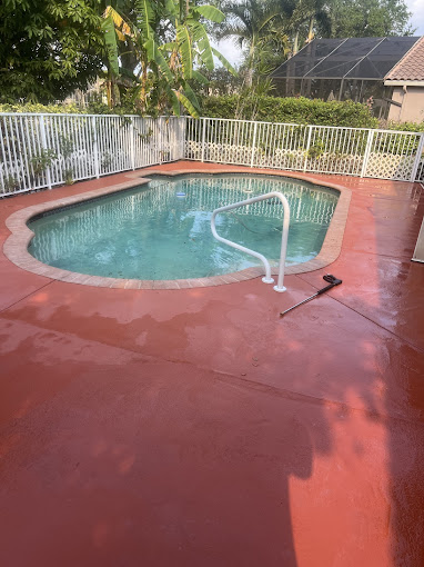 Kidney-shaped pool with blue water and white fence on red concrete deck