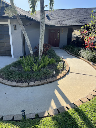Curved concrete walkway leading to a gray house with landscaped garden