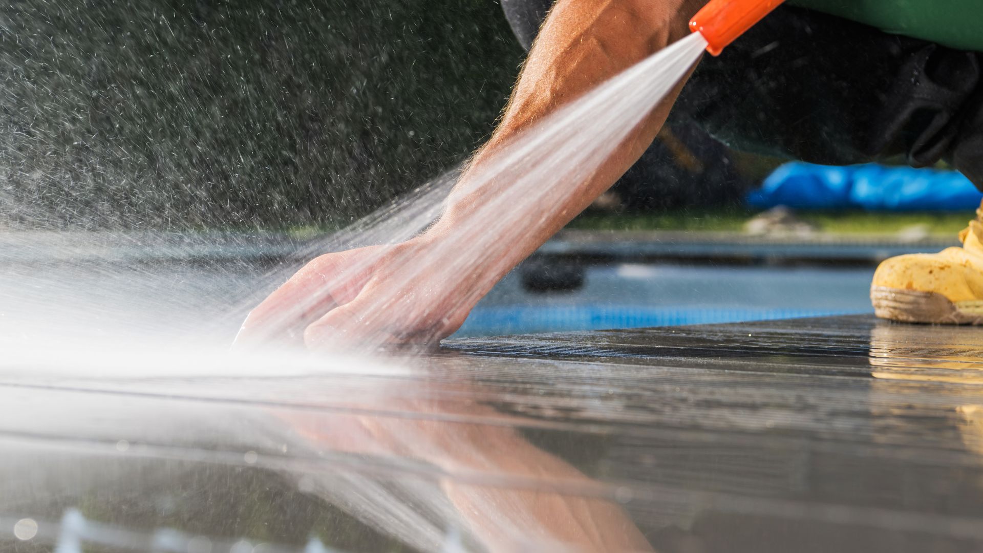 Hand using orange-handled spray nozzle to wash surface with water spray