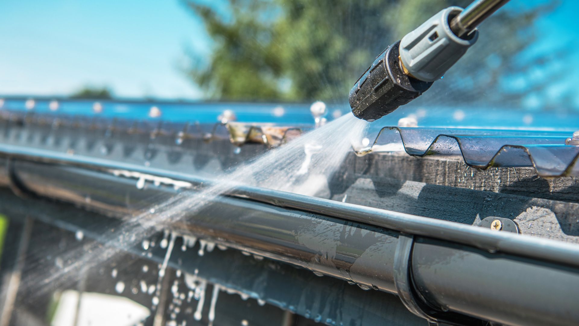 Pressure washer cleaning metal gutter with high-pressure water spray